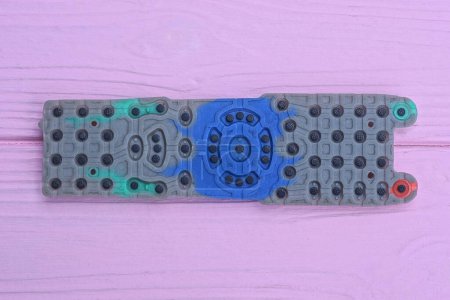 one long colored rubber gasket of a television remote control lies on a pink wooden table