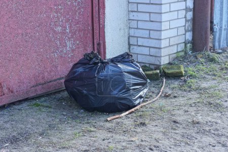 one black plastic bag with garbage stands on the gray ground on the street