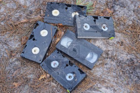 a pile of five black plastic dirty old video cassettes lie on the gray ground on the street
