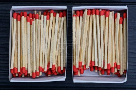 deux boîtes ouvertes en papier avec des allumettes en bois gris et des têtes rouges reposent sur une table noire