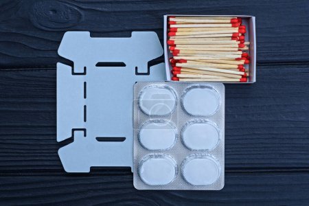 a set of gray metal portable burner packs with white dry alcohol fuel and matches lies on a black wooden table
