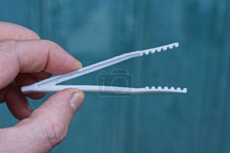 Photo for Fingers holding one white plastic tweezers on a green background - Royalty Free Image