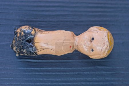 un petit jouet de poupée brisée en plastique brun carbonisé repose sur une table en bois noir