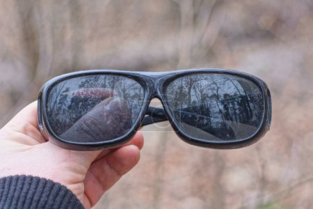Téléchargez les photos : Main tient une lunettes de soleil en plastique noir sur fond gris - en image libre de droit