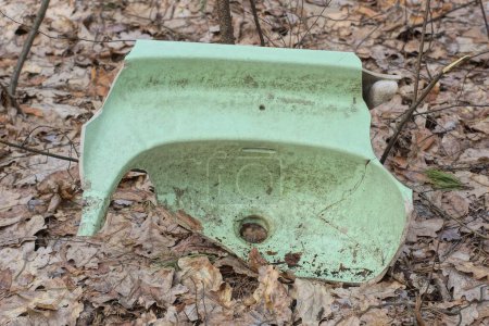 one green dirty broken old ceramic washbasin with a hole lies on the gray ground on the street