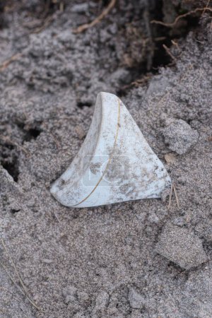 Ein weißes Stück Keramik aus einer alten zerbrochenen Tasse liegt im grauen Sand auf der Straße