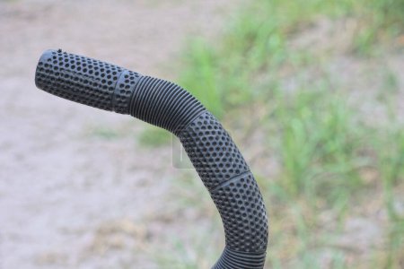 one black plastic grip on the handlebars of a bike outdoors on a gray background