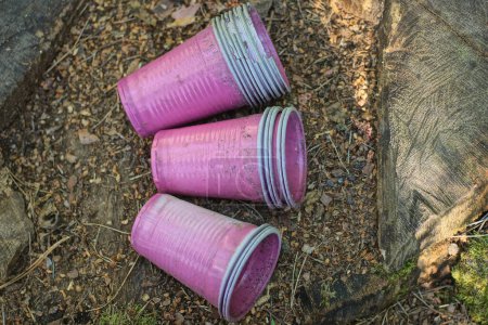 a row of old dirty purple plastic cups lie on the gray ground outside
