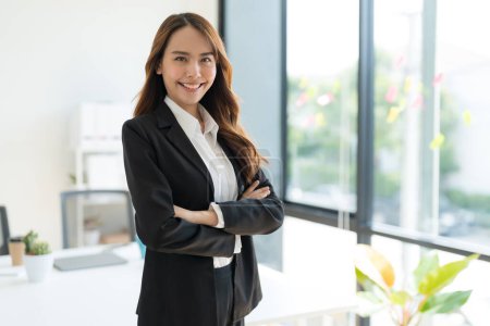 Young businesswoman standing with crossed arms smiling and wearing a black suit standing in the office.