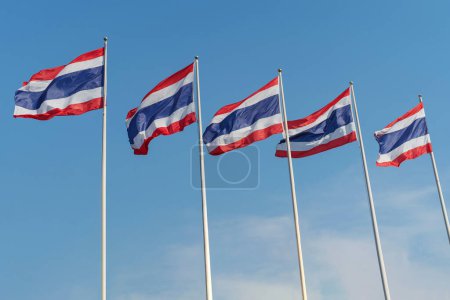 The national flags of Thailand flutter against a blue sky.