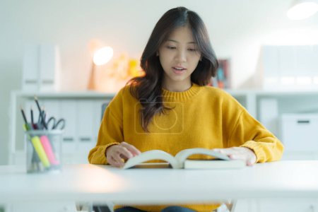 Foto de Una joven o estudiante leyendo un libro en la biblioteca mientras lleva gafas, Ella sonríe y se ve feliz. - Imagen libre de derechos