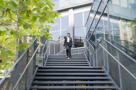 Professional woman in suit walks down steps outside a modern office building