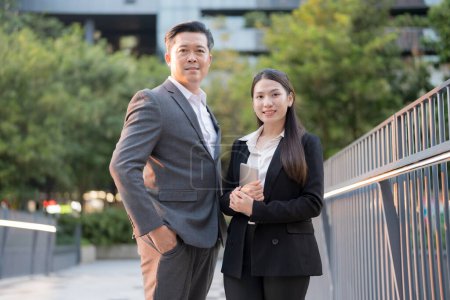 Téléchargez les photos : Homme et femme professionnels debout en toute confiance à l'extérieur avec des immeubles de bureaux en toile de fond - en image libre de droit