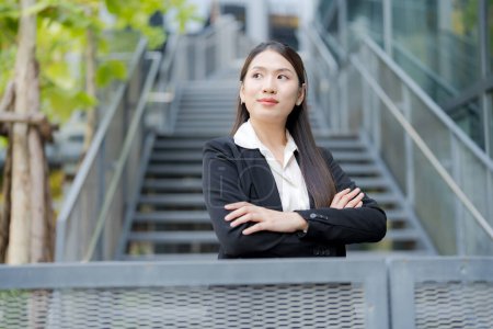 Young asian professional businesswoman smiling confidently in an urban environment. Wearing modern business attire. Showcasing elegance and positivity. In front of an office building staircase