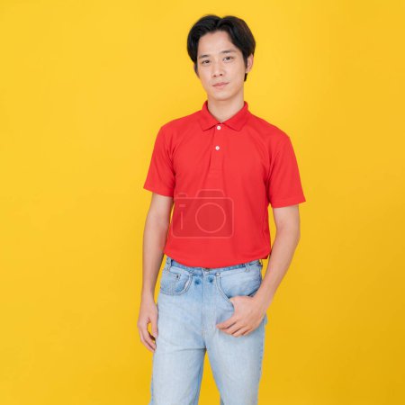 Young adult male stands confidently with hands in denim pockets, wearing a vibrant red polo shirt against a striking yellow background, embodying casual style and positive body language