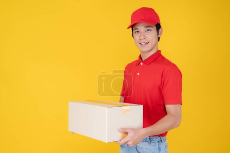 Foto de La persona de entrega enfocada en un uniforme rojo y una gorra sostienen con confianza un paquete, listo para proporcionar un servicio rápido contra un fondo amarillo vibrante - Imagen libre de derechos
