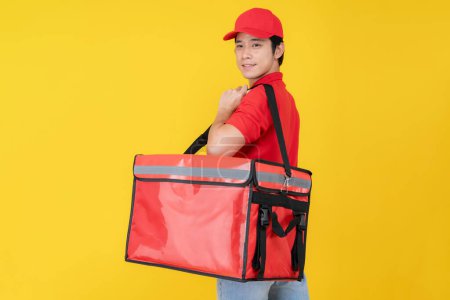 Portrait of a smiling young delivery man wearing a red cap and polo shirt, holding an insulated food delivery bag against a vibrant yellow background, symbolizing efficient food delivery service