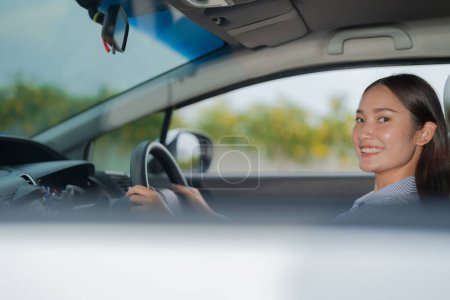Lächelnde junge Frau auf dem Fahrersitz, selbstbewusst das Lenkrad eines Autos mit einem hellen und fröhlichen Gesichtsausdruck, der sicheres und angenehmes Autofahren hervorhebt