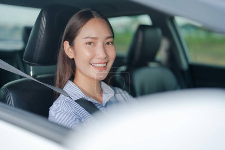 Téléchargez les photos : Jeune femme souriante assise sur le siège du conducteur, tenant en toute confiance le volant d'une voiture avec une expression lumineuse et joyeuse, soulignant une conduite sûre et agréable - en image libre de droit