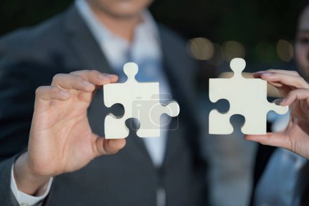 Nahaufnahme mit zwei Profis, die große Puzzleteile in der Hand halten, die für Zusammenarbeit, Problemlösung und Partnerschaft in Richtung eines gemeinsamen Ziels im Unternehmensumfeld stehen