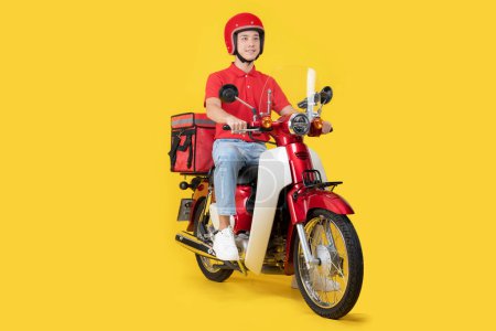 Cheerful asian delivery man in a red polo shirt and helmet rides a red motorcycle, equipped with a thermal backpack for food delivery, isolated on a bright yellow background