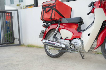Rotes Liefermotorrad mit einer großen, isolierten Lebensmittelbox, die auf einer Straße geparkt ist und moderne Essenslieferdienste in einer städtischen Umgebung präsentiert