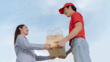 Smiling young woman receives a cardboard box from a friendly delivery man outdoors, portraying excellent customer service and efficient doorstep delivery with a personal touch