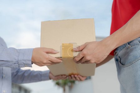 Mujer joven sonriente recibe una caja de cartón de un hombre de entrega amigable al aire libre, retratando un excelente servicio al cliente y una entrega eficiente en la puerta con un toque personal
