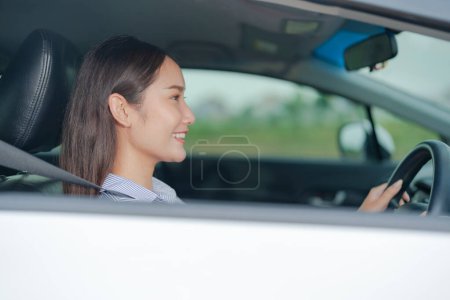 Téléchargez les photos : Jeune femme souriante assise sur le siège du conducteur, tenant en toute confiance le volant d'une voiture avec une expression lumineuse et joyeuse, soulignant une conduite sûre et agréable - en image libre de droit