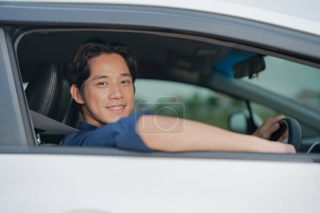 Foto de Joven, conductor masculino sonriente se representa con confianza al volante de un vehículo moderno, exudando una sensación de libertad y satisfacción mientras conduce su coche - Imagen libre de derechos