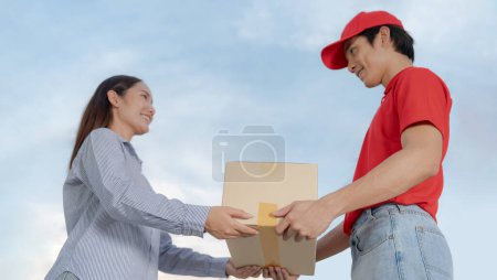 Mujer joven sonriente recibe una caja de cartón de un hombre de entrega amigable al aire libre, retratando un excelente servicio al cliente y una entrega eficiente en la puerta con un toque personal