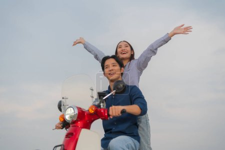 Junges asiatisches Paar in lässiger Kleidung genießt eine lustige Fahrt auf einem roten Motorrad auf offener Straße, wobei sich die Frau frei und glücklich fühlt