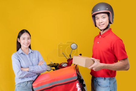 Fröhliche junge Frau erhält ein Paket von einem freundlichen Kurier mit Helm, während sie an einem roten Liefermotorrad vor leuchtend gelbem Hintergrund steht