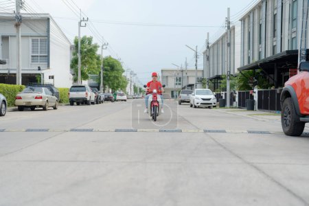 Foto de Joven repartidor sonriente con gorra roja montando una moto ecológica en una calle urbana, mostrando servicios de entrega modernos y soluciones sostenibles de transporte urbano - Imagen libre de derechos