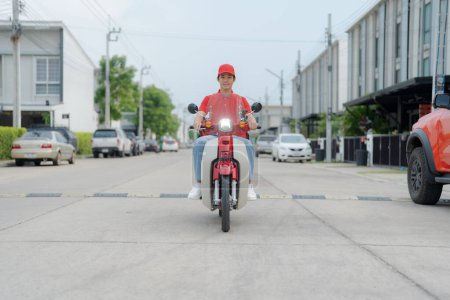 Lächelnder junger Lieferant mit roter Mütze, der auf einem umweltfreundlichen Motorrad eine urbane Straße hinunterfährt und moderne Lieferdienste und nachhaltige Lösungen für den städtischen Verkehr präsentiert