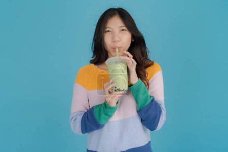 Foto de Joven alegre en un suéter colorido sorbe té de burbuja a través de una paja sobre un fondo azul brillante, encarnando un momento despreocupado y refrescante - Imagen libre de derechos