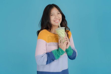 Foto de Joven alegre en un suéter colorido sorbe té de burbuja a través de una paja sobre un fondo azul brillante, encarnando un momento despreocupado y refrescante - Imagen libre de derechos