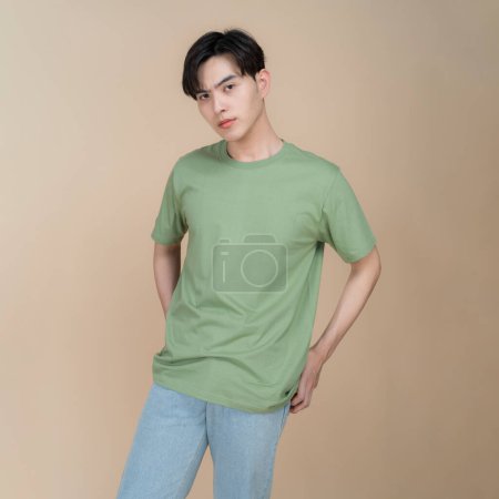 Foto de Elegante joven posa con confianza en una camiseta verde lisa y vaqueros azules sobre un fondo beige neutro, perfecto para maquetas de moda y ropa - Imagen libre de derechos