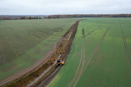 Drone photography of excavator cleaning drainage ditch in an agriculture field during autumn cloudy morning