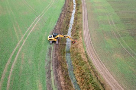 Drone photography of excavator cleaning drainage ditch in an agriculture field during autumn cloudy morning