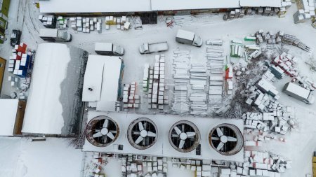 Foto de Fotografía de drones de ventiladores de refrigeración a escala industrial y material de construcción en un almacén al aire libre cubierto de nieve durante el día nublado de invierno - Imagen libre de derechos