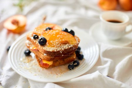Photo for Breakfast on white bed sheets, good morning, summer french toast with cream cheese, honey, peaches and blueberries, coffee, flowers, Hotel room early morning, honeymoon - Royalty Free Image