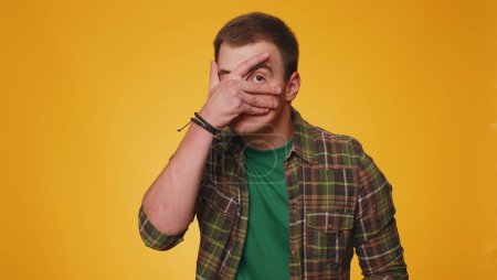Dont want to look at this, awful. Handsome shocked teen man closing eyes with hand showing stop gesture, confused shy scared to watch. Young adult guy boy isolated alone on yellow studio background