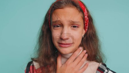 Photo for Upset disappointed young teenager child girl kid 12 years old wipes tears and cries from despair, being sad because of unfair things, broken love. Preteen children isolated on studio blue background - Royalty Free Image