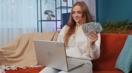 Photo for Planning budget. Rich happy young woman counting money cash use laptop pc calculate domestic bills at home. Joyful student girl satisfied of income earnings, saves money for planned vacation, gifts - Royalty Free Image