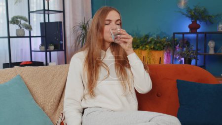 Téléchargez les photos : Portrait of thirsty lovely girl sitting indoors holding glass of natural aqua make sips drinking still water preventing dehydration. Woman with good life habits, healthy slimming, weight loss concept - en image libre de droit