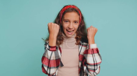 Foto de Joven adolescente niña niño gritando, levantando los puños en el gesto lo hice, celebrando el éxito, ganar, cumpleaños, lotería lotería Logros objetivo. Niños preadolescentes aislados en el fondo azul del estudio - Imagen libre de derechos