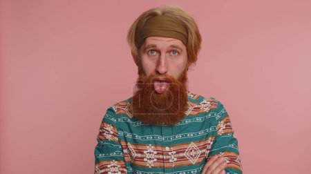 Photo for Funny joyful sincere redhead hippie man in pattern shirt making playful silly facial expressions and grimacing, fooling around showing tongue. Young handsome hipster guy isolated on pink background - Royalty Free Image
