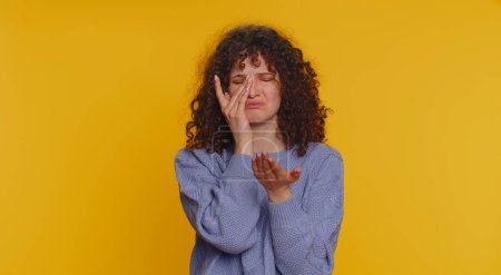Photo for Upset disappointed young curly haired woman wipes tears and cries from despair, being sad because of unfair things. Teen girl in depression, despair, loss isolated alone on yellow studio background - Royalty Free Image