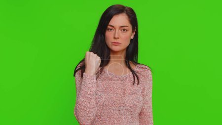 Téléchargez les photos : Angry aggressive woman trying to fight at camera, shaking fist, boxing with expression, punishment, disappointment, rage, quarrel. Young adult girl isolated alone on green screen chroma key background - en image libre de droit